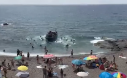 WATCH: Beachgoers flee as dozens of migrants leap from boat and charge ashore at tourist hotspot