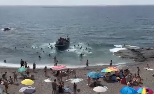 WATCH: Beachgoers flee as dozens of migrants leap from boat and charge ashore at tourist hotspot